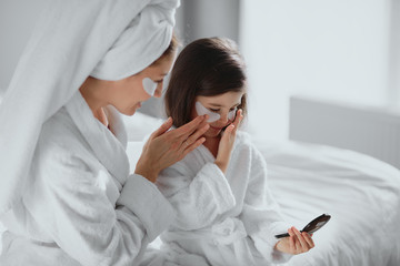 beautiful mother in bathrobe and her little daughter together with towels on head and mask on face...