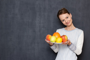 Portrait of happy young woman holding plate with ripe fresh fruits