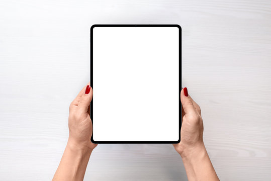 Tablet mockup. Girl holding tablet in vertical position abowe white desk. Flat lay, top view
