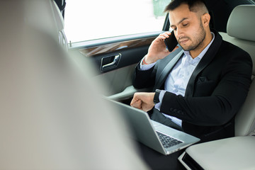 Fototapeta premium confident businessman looking at wristwatches busy with work, talking with business colleague in executive car