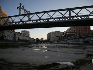 Dry riverbed of the Guadalmedina river in Málaga, Spain, with just a few small streams or puddles of water on the concrete ground and grass