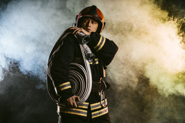 handsome fireman in helmet stand isolated in smoky space, wearing uniform. safety