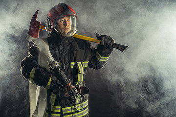 young caucasian fireman holding hammer, risking his life to save people from fire, wearing protective uniform