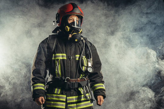 brave extinguisher or fireman dressed in dark protective suit uniform, with helmet on head, using ropes, hammer and other special equipment at work