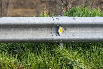 close up of guardrail with yellow reflector and Grass on the road