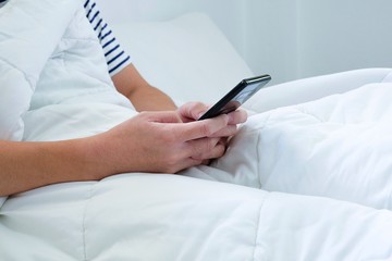 Asian men hand using smartphone texting and web browsing internet on white bed and blanket. Technology lifestyle daily routine of urban city people with copy space for text.