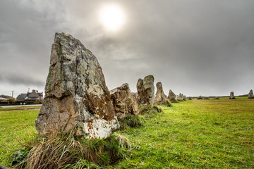 Standing stones in Brittany. Alignment of menhirs on a green meadow and under a gray sky. - obrazy, fototapety, plakaty