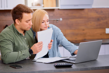 couple checking analyzing utilities bills sitting together at kitchen table, husband and beautiful...