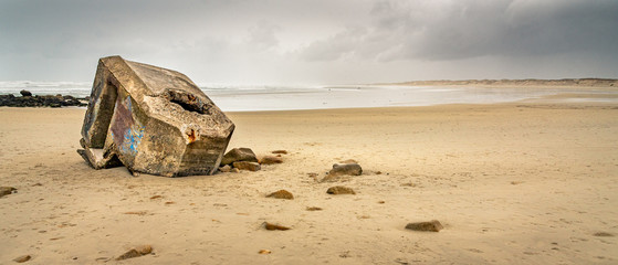 La Torche beach in Brittany in winter. The ruins of an old German WWII bunker seem stranded on the beach under a threatening rain sky