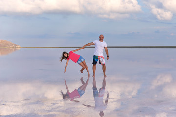 Young father with teenage daughter holding hands standing in salt lake, reflected in water