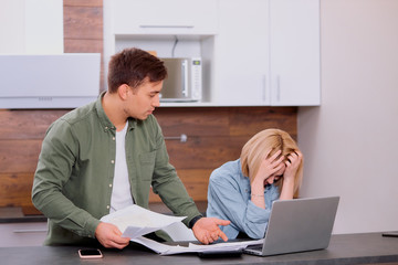 couple using modern laptop computer, looking worried and sad, studying online, solving financial problems at home, anxious, searching for job, reading bad news, searching, talking, using papers