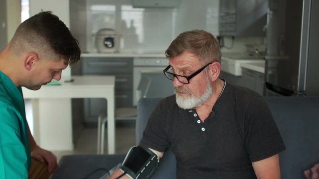 Blood pressure measurement. An elderly patient and a young doctor during a blood pressure measurement procedure with a tonometer at home in a patient. Hypertension, healthcare concept