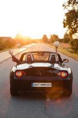 Wedding Just Married sign black rodster cabrio coupe car with bride and groom leaving into sunset...
