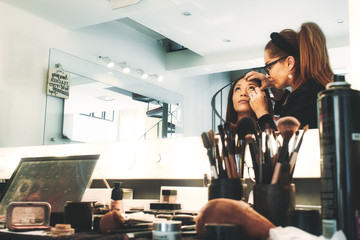 A professional makeup artist in a studio painting a woman's face