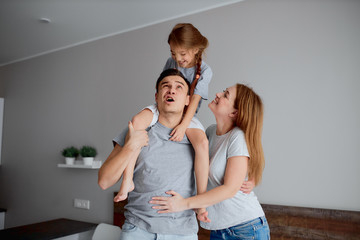 playful caucasian couple full of emotions stand isolated in bedroom at home, kid girl sit on shoulders of strong father, wearing casual clothes