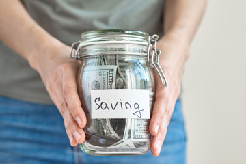 Woman hands holding glass jar with inscription saving full of a dollar banknotes. Saving money and home budget concept