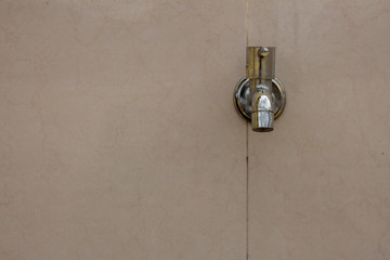 Stainless steel water tap fixed to tiled wall in building exterior.