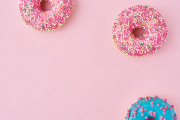 Different types of a colorful donats decorated sprinkles and icing on pastel pink background with copy space