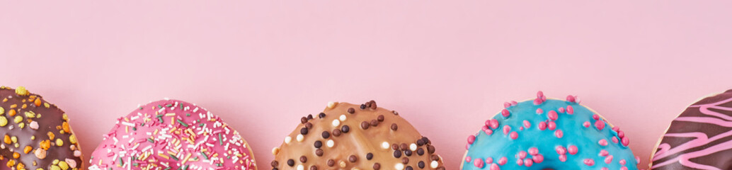 Halfs of different types colorful donats decorated sprinkles and icing on a pastel pink background, long banner