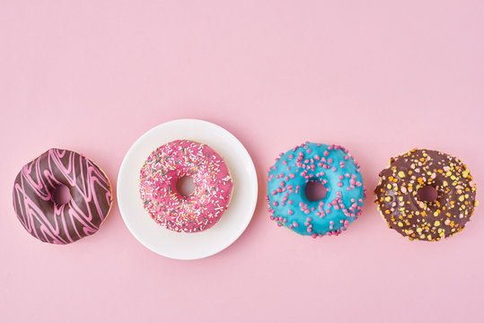 Different colorful donuts and plate on the pink background. Creative food concept