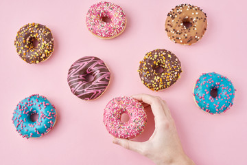 Woman hand take color donut on a pink background. Creativity minimalism style food concept, top view