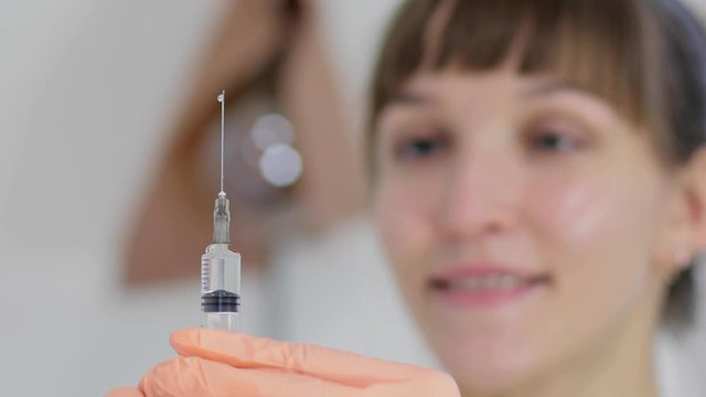 The doctor&rsquo;s hands release excess air from the syringe, the doctrine smiles and suggests not to be afraid of injections. Soft focus, close up.