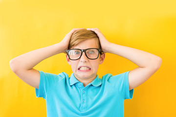 Frustrated boy holding his head on a yellow background. Study, difficulties and problems concept
