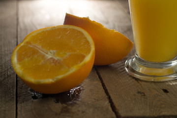 Glass of fresh orange juice with cut oranges on wooden background