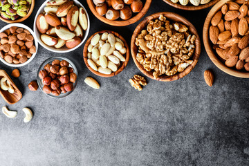Obraz na płótnie Canvas Mix nuts in wooden bowls on dark stone table top view. Almonds, pistachio, walnuts, cashew, hazelnut.