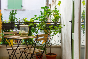 An Italian balcony with green potted plants and garden furniture. a table and chairs to enjoy the...