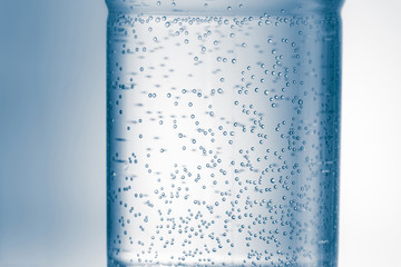 Close-up fragment of plastic bottle full of water with air bubbles against light blue  background.