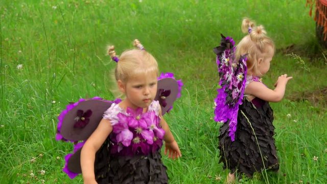 Two girls in a violet butterfly costumes walking on the green lawn. Children pretend to be purple butterflies