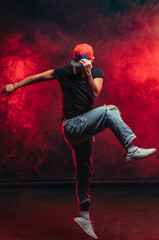 young good-looking stylish man 20-25 years old dancing street dance isolated over smoky background,...