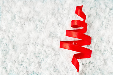 Silk red ribbon twisted in the form of a Christmas tree in the snow. Background for greeting card, poster, banner or invitation for the new year 2020. Copy space.