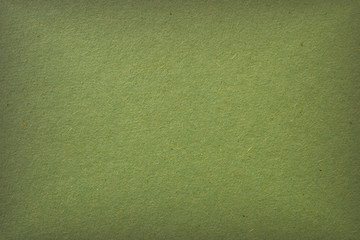 The surface of a sheet of green cardboard. Calm relaxing background or wallpaper. Rough natural paper texture with cellulose fibers. Square vignetting fogging around the edges. View from above. Macro