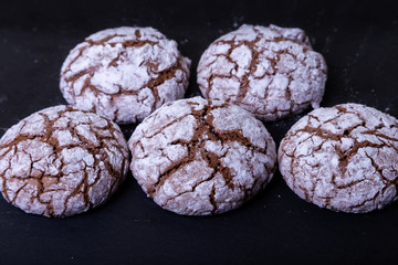 Chocolate cookies with cracks, strewed with icing sugar. Homemade baking, dark background. Selective focus, close-up.