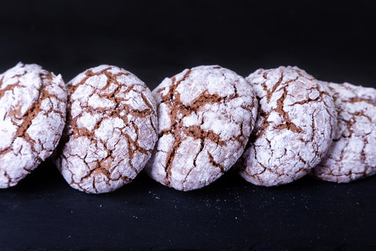 Chocolate cookies with cracks, strewed with icing sugar. Homemade baking, dark background. Selective focus, close-up.