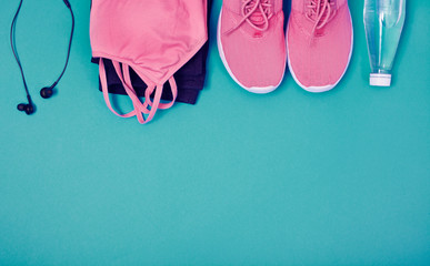 Pair of pink sport shoes, earphones, bottle of water, leggings and sport crop top on a azure background. Concept of healthy lifestyle, sport and diet. Copy space. Top view.