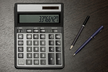 Calculator, pen and pencil on dark office table. View from above.