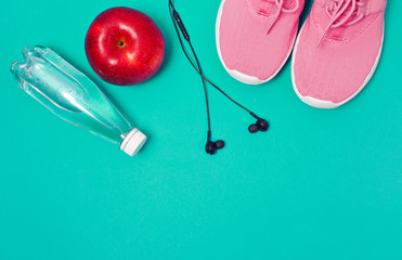 Pink sport shoes, earphones, red apple and bottle of water on a blue background. Concept healthy lifestyle, sport and diet. 