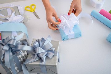 Woman wraps boxes with gifts for the new year. Female hands close-up. Prepares a surprise for mother's day. Wrapping paper and ribbon for birth. The designer is tying a bow.