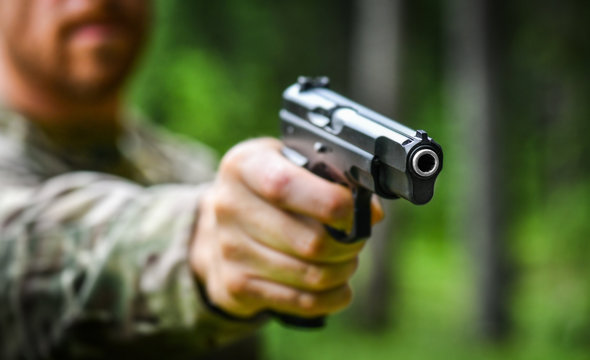Army man hold a 9mm gun prepare to fire on target. Guns an ammunition weapon detail. Blur or defocus background.