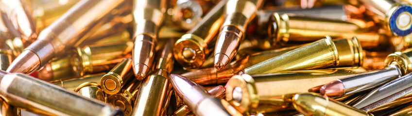 Pile of fire bullets or ammunition banner or panorama on dark stone table.  Hand guns weapon in background. Many projectiles into 9mm gun. - obrazy, fototapety, plakaty