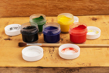 Open jars of gouache paint on a wooden background. Nearby lies a brush.