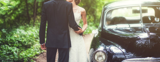 Luxury wedding couple embracing near retro car