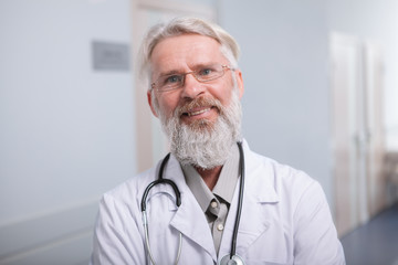 Close up of a happy senior bearded doctor smiling to the camera, working at the clinic