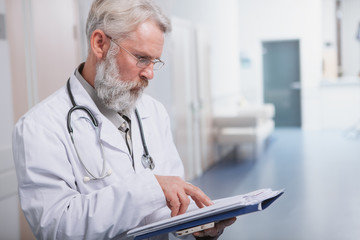 Cropped shot of a senior male doctor concentrating, reading medical documents on his clipboard, copy space