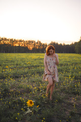 Fototapeta premium Beautiful redhead woman in a summer short dress during Golden Hour in a sunflower field in Eastern Europe Latvia Smarde