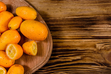 Cutting board with kumquat fruits on wooden table. Top view