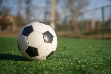 A black and white soccer ball on an artificial turf on a clear sunny day.